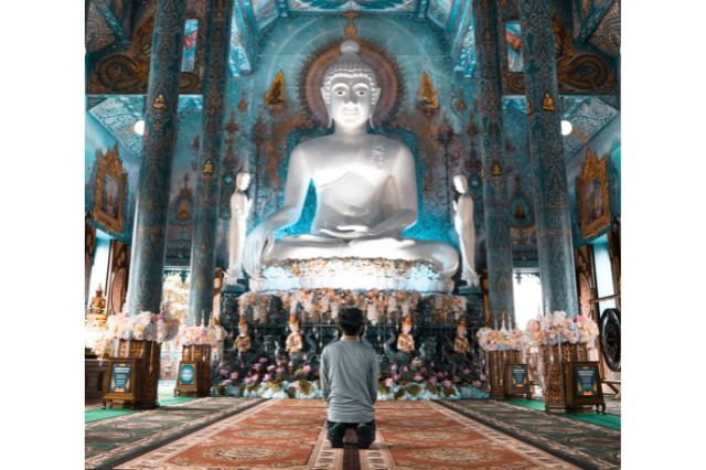 man kneeling in prayer before a Buddha statue